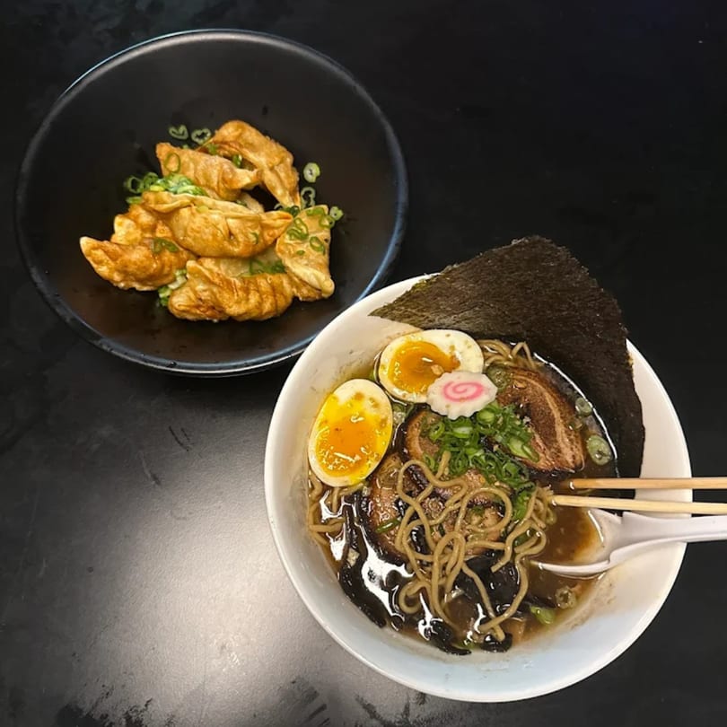 A bowl of Frankie Ramen with pork, egg, and seaweed, alongside a plate of gyoza.