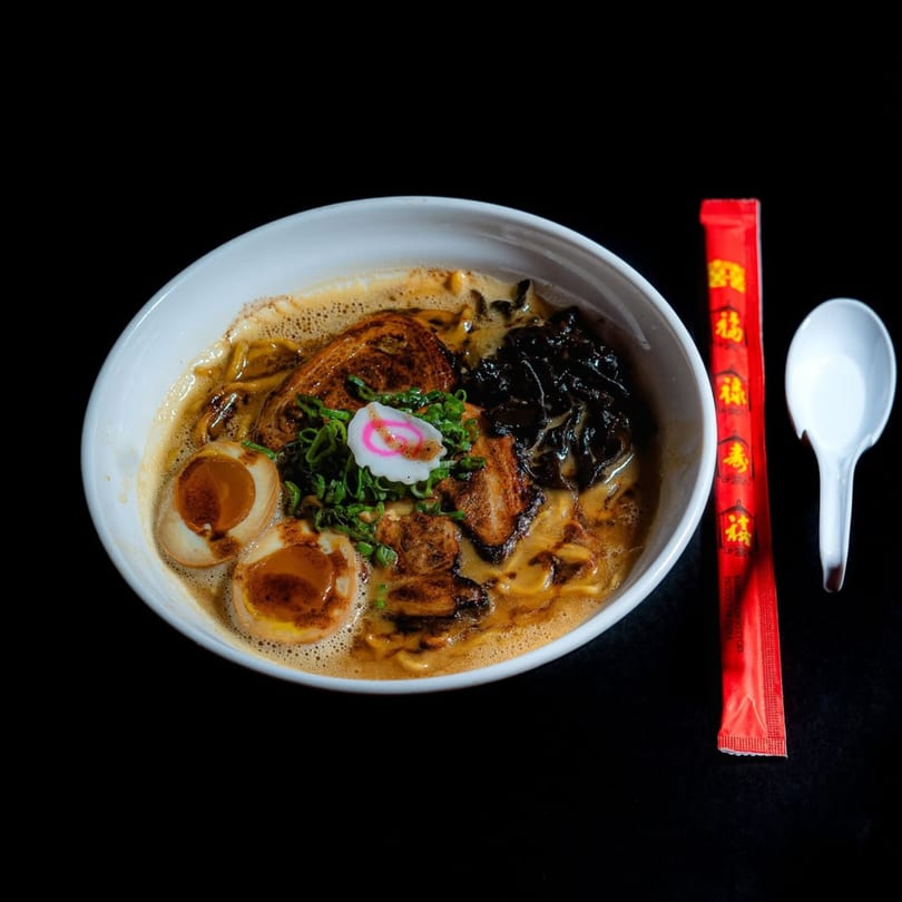 A bowl of Frankie Ramen with pork, eggs, mushrooms, green onions, and a fish cake.