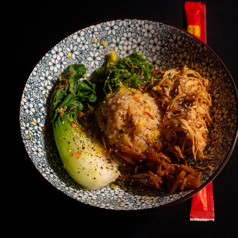 A bowl of Frankie Ramen's ramen with shredded chicken, bok choy, rice, and greens.