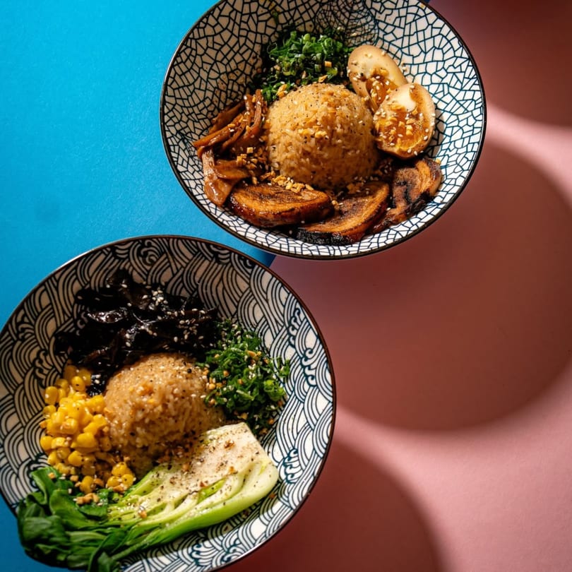 Two bowls of Frankie Ramen's ramen, one with eggs and mushrooms, the other with corn and bok choy.