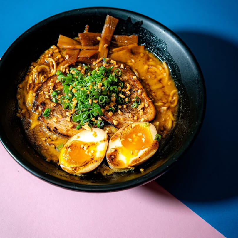 A bowl of Frankie Ramen with pork, soft-boiled eggs, bamboo shoots, and green onions.