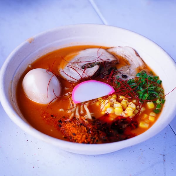 A bowl of Frankie Ramen with pork, egg, corn, scallions, and a pink fish cake.