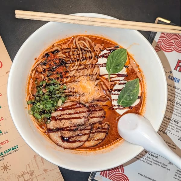 A bowl of Frankie Ramen's ramen with pork, noodles, broth, green onions, and basil.