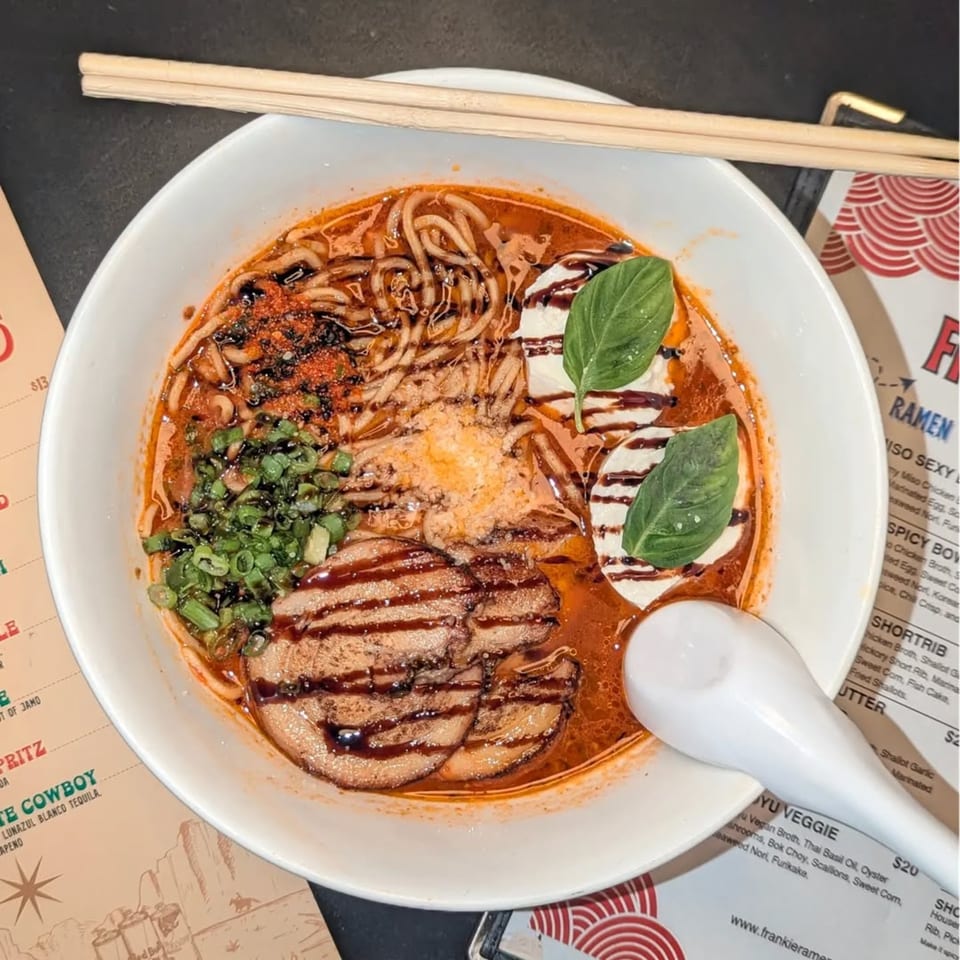 A bowl of Frankie Ramen's ramen with pork, noodles, broth, green onions, and basil.