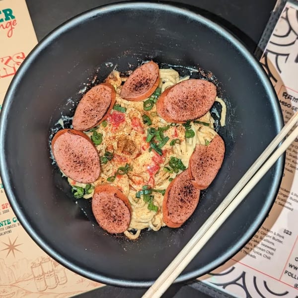 Frankie Ramen's creamy ramen with sliced sausage, green onions, and red spices in a black bowl.